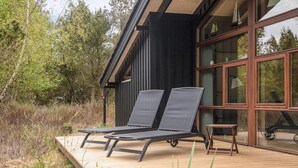 A modern house with a deck, two lounge chairs, and a small table. - 5 Star Holiday Home in Fjerritslev (Fjerritslev)