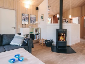 A cozy living room with a fireplace, wooden walls, a sofa, a coffee table, and a bookshelf. - 5 Star Holiday Home in Fjerritslev (Fjerritslev)