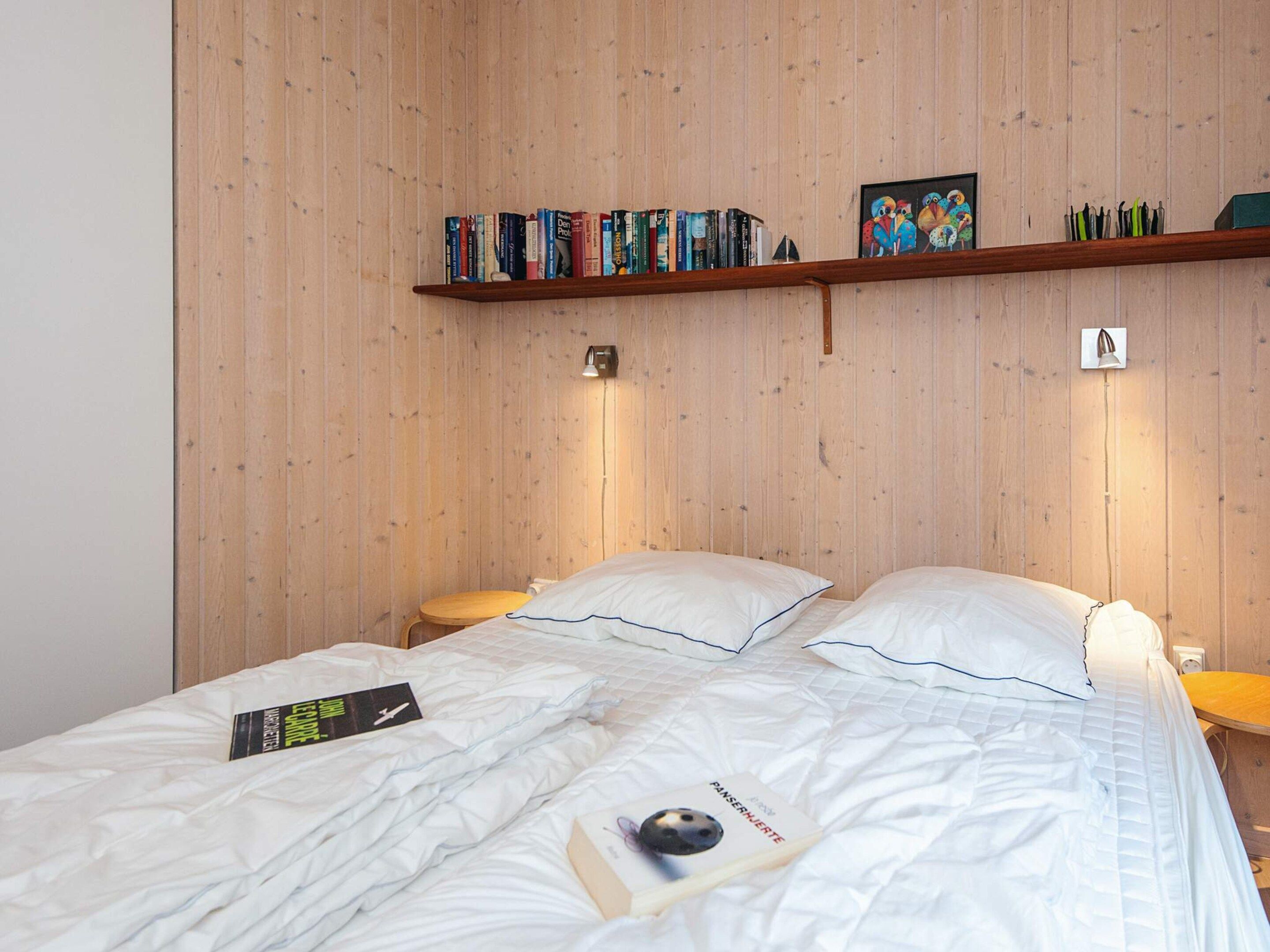 A bedroom with two beds, wooden panel walls, a bookshelf, and a framed picture.