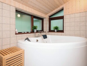 A modern bathroom with a freestanding bathtub, wooden slatted bench, and two windows with potted plants. - 5 Star Holiday Home in Fjerritslev (Fjerritslev)