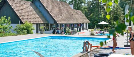 A swimming pool area with lounge chairs and a building with a sloped roof.