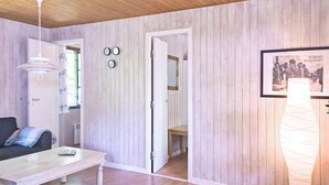 A room with wooden panel walls, a white door, a small table with a remote control, and a framed picture on the wall. - 6 Person Holiday Home in Nexo (Nexø)