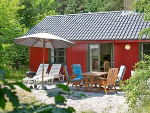 A red building with a tiled roof, outdoor seating with chairs and a table, and a barbecue grill. - 6 Person Holiday Home in Nexo (Nexø)