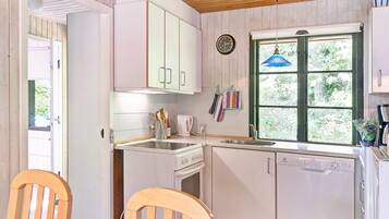 Una cocina con armarios blancos, estufa, pileta y ventana con vista a follaje.