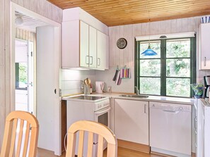 A kitchen with white cabinets, a stove, a sink, and a window with a view of greenery. - 6 Person Holiday Home in Nexo (Nexø)