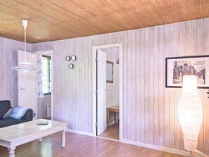 A room with wooden panel walls, a white door, a white table with a remote control, and a framed picture on the wall. - 6 Person Holiday Home in Nexo (Nexø)