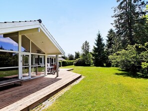Een modern huis met een overdekt terras, een gazon en een grote boom.