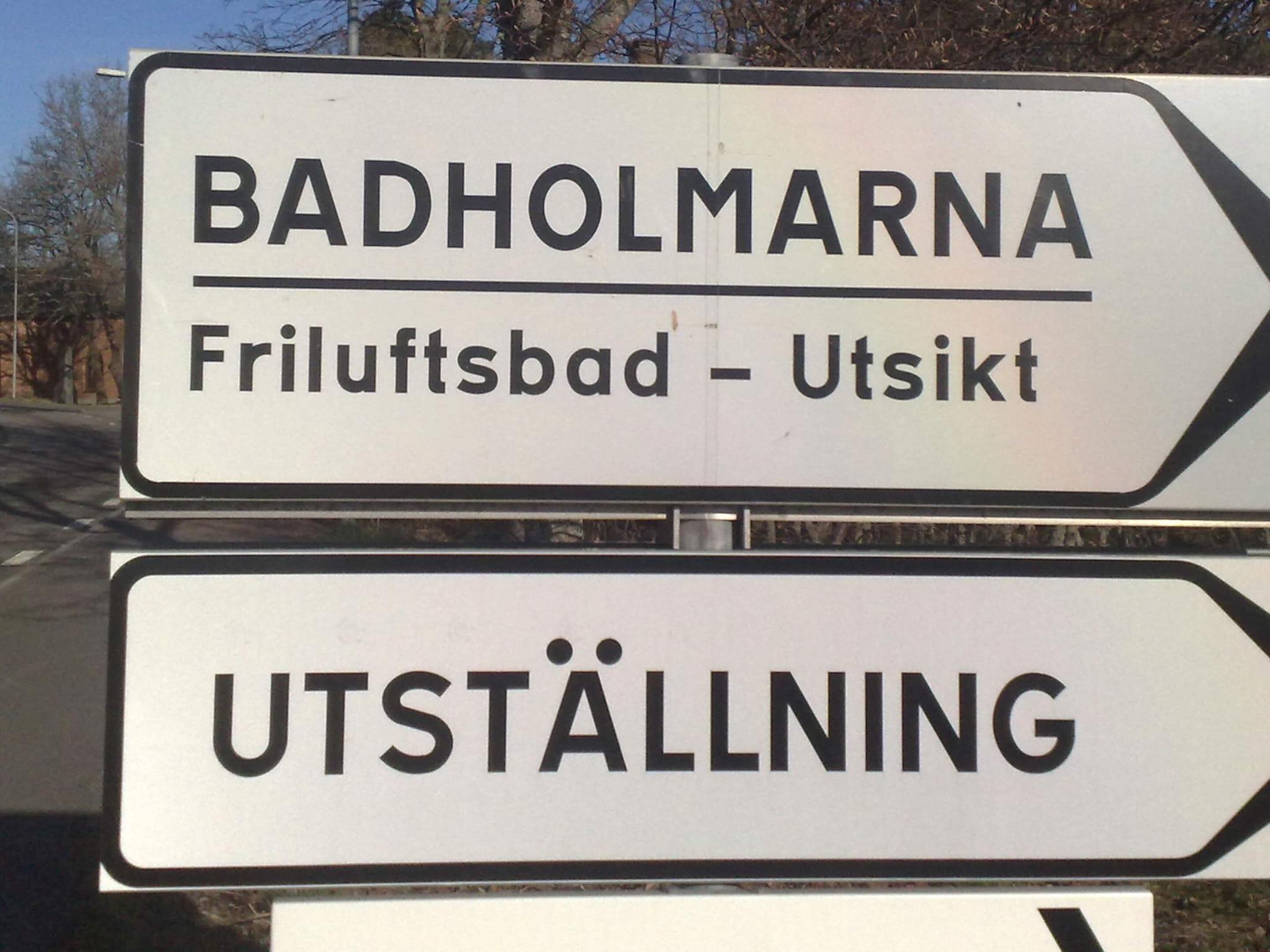 A directional sign with the text "BADHOLMARNA Friluftsbad - Utsikt" and "UTSTÄLLNING".
