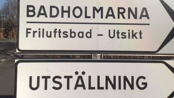 A directional sign with the text "BADHOLMARNA Friluftsbad - Utsikt" and "UTSTÄLLNING".