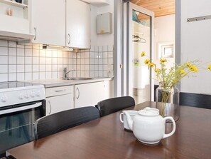 A modern kitchen with white cabinets, a stove, and a sink. There is a wooden table with a white teapot and a vase of yellow flowers.