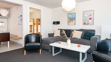 Ein modernes Wohnzimmer mit einem grauen Sofa, schwarzen Ledersesseln, einem weißen Couchtisch und einer hängenden Leuchte.