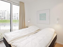 Habitación de hotel con cama, ventana con cortinas, una lámpara de pared y un cuadro enmarcado.