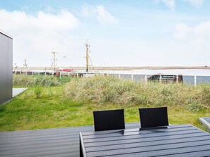 En træterrasse med to stole, der kigger ud over et vandareal med både og en fjerntliggende kystlinje.