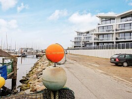 A waterfront property with a modern building, a marina with boats, and a car parked on the street.