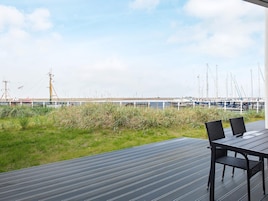 Una terraza con mesa y sillas que da a un puerto deportivo con barcos y una costa lejana.