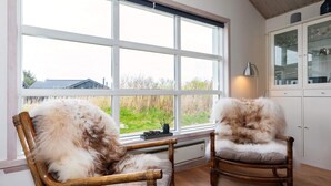 Dos sillas de mimbre con cojines blancos mullidos en una habitación con un ventanal grande, suelo de madera y un aparador con puertas de vidrio.