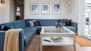 Una sala de estar moderna con un sofá seccional azul, una mesa de centro de vidrio y tres obras de arte enmarcadas en la pared.