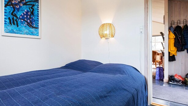 Un dormitorio con una cama grande, una lámpara de pared y una puerta que da a un pasillo con abrigos y zapatos.