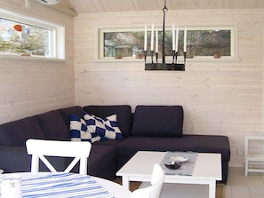 A cozy room with a dark-colored sofa, a white chair, a small table with a striped tablecloth, and a window with a candle holder. - Holiday Home in KÃ¥llekärr (Kållekärr)