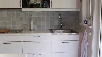 Una cocina con horno empotrado, pileta de acero inoxidable y ventana con una toalla colgada en la puerta.