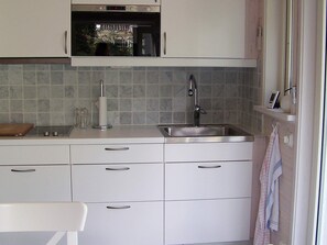A kitchen with a built-in oven, a stainless steel sink, and a window with a towel hanging on the door. - Holiday Home in KÃ¥llekÃ¤rr (Kållekärr)