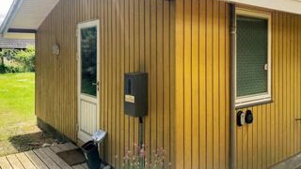 Ein Holzgebäude mit einer Tür, einem Fenster und einem kleinen schwarzen Gegenstand an der Wand.