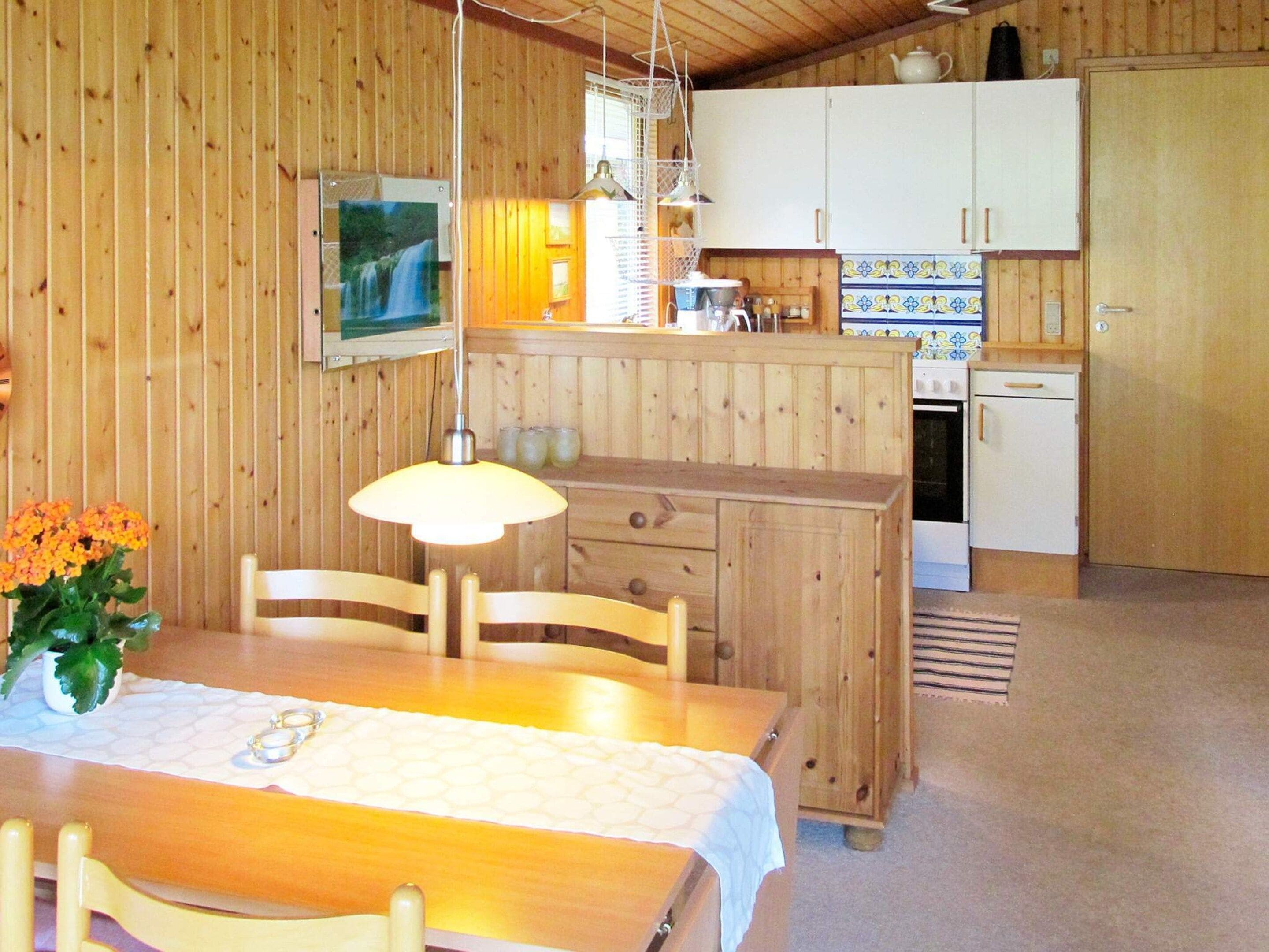 A wooden interior with a dining table, chairs, a kitchen area with cabinets, and a hanging light fixture.