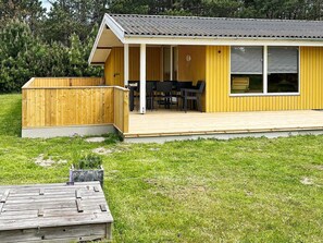 A yellow building with a wooden deck, a covered patio area, and a window with blinds. - 4 Person Holiday Home in Rodby (Rodby)