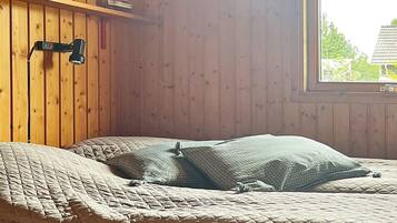 A room with a bed, wooden walls, a window, and a shelf with items.