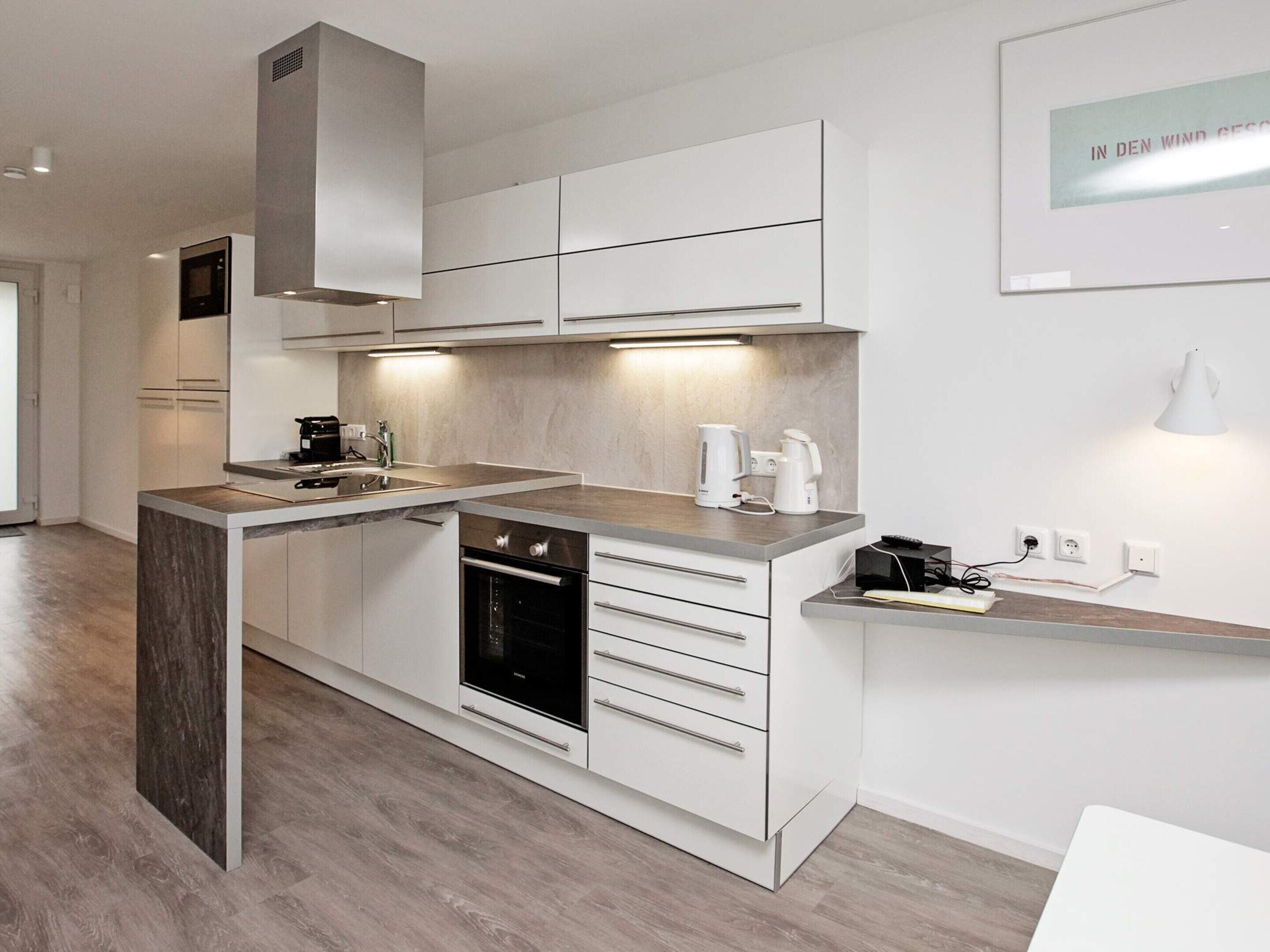 A modern kitchen with a built-in oven, a coffee maker, and a kettle on the countertop.