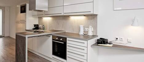 A modern kitchen with a built-in oven, a coffee maker, and a kettle on the countertop.