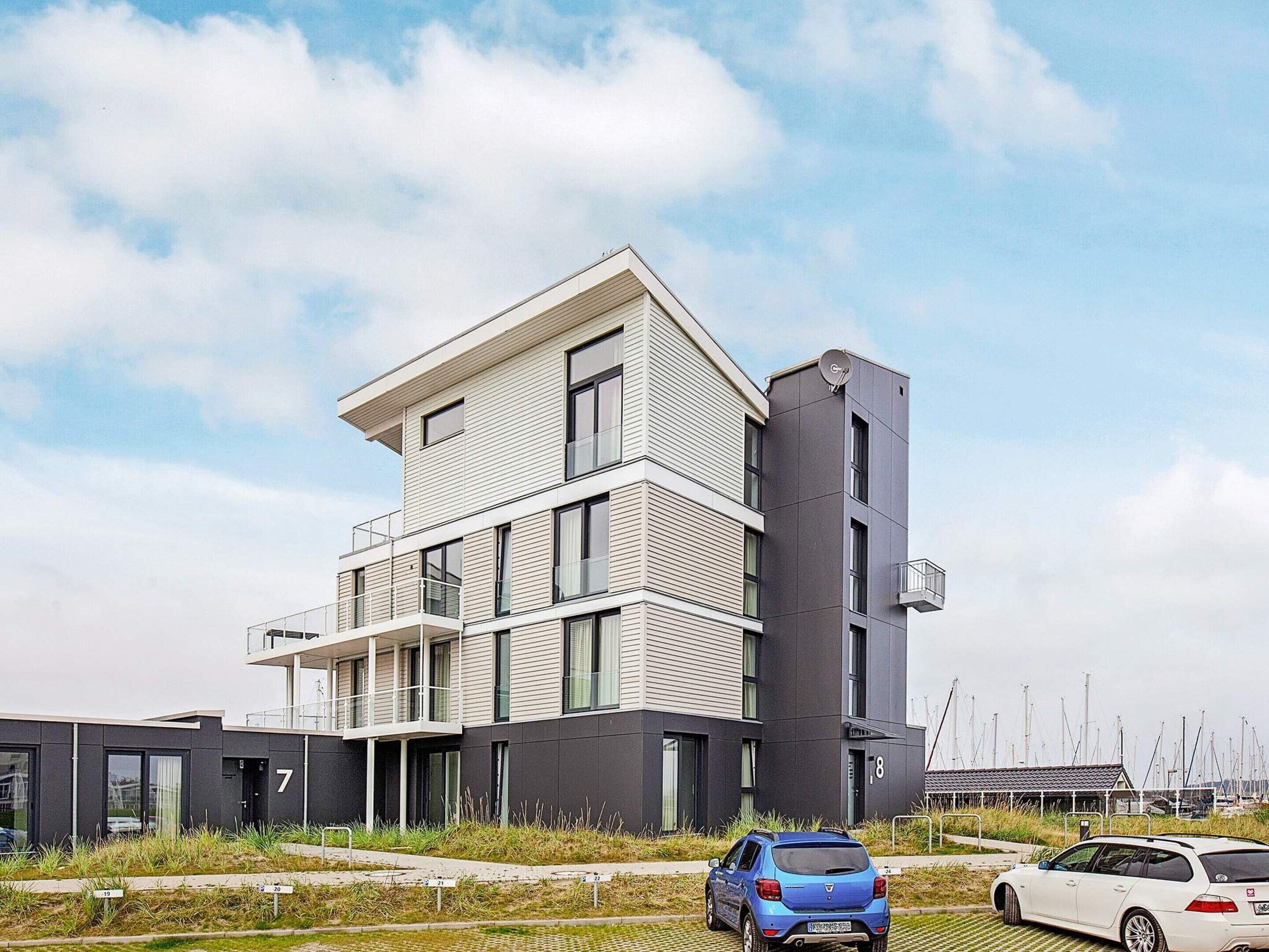 A modern multi-story building with balconies, a satellite dish, and a marina in the background.