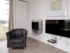 A modern living room with a dark armchair, a wall-mounted TV, and a framed map.