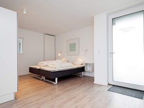 A modern bedroom with a bed, bedside lamps, a framed picture, and a door with a frosted glass panel. - Holiday Home in Wendtorf (Wendtorf)