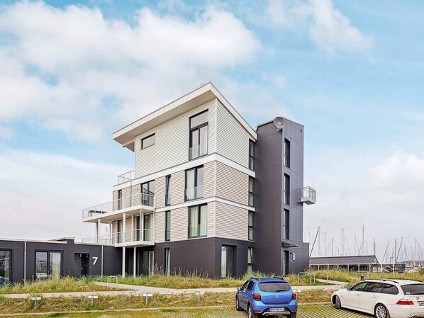 A modern multi-story building with balconies, a satellite dish, and a marina in the background. - Holiday Home in Wendtorf (Wendtorf)
