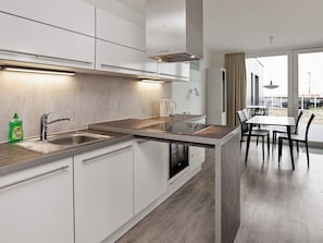 A modern kitchen with a built-in oven, a sink, and a dining area with a table and chairs. - Holiday Home in Wendtorf (Wendtorf)