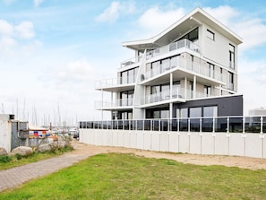 A modern multi-story building with balconies, a paved pathway, and a grassy area. - Holiday Home in Wendtorf (Wendtorf)