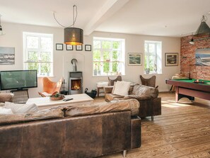 A cozy living room with a fireplace, leather sofas, a pool table, and a television.