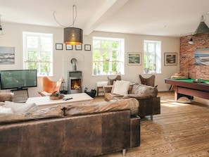 A cozy living room with a fireplace, leather sofas, a pool table, and a television.