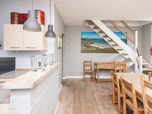 A modern kitchen with wooden cabinets, pendant lights, and a dining area with a wooden table and chairs.