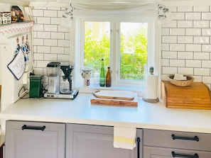 A kitchen with a window, a coffee maker, a cutting board, and a basket on the counter.