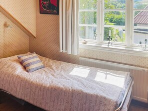 A single bed with a patterned bedspread, a window with curtains, and a radiator below. - 4 Person Holiday Home in Ronnang (Roennaeng)