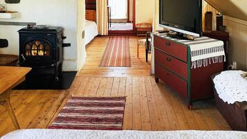 A cozy room with a bed, a television, a dresser, a red bench, a wooden floor, and a fireplace.