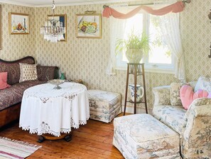 A traditional room with patterned wallpaper, a round table with a white tablecloth, a sofa, a floral armchair, and a potted plant by the window. - 4 Person Holiday Home in Ronnang (Roennaeng)