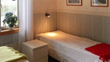 Una cama individual con una colcha roja, una mesita de noche, una lámpara y una ventana con cortinas.