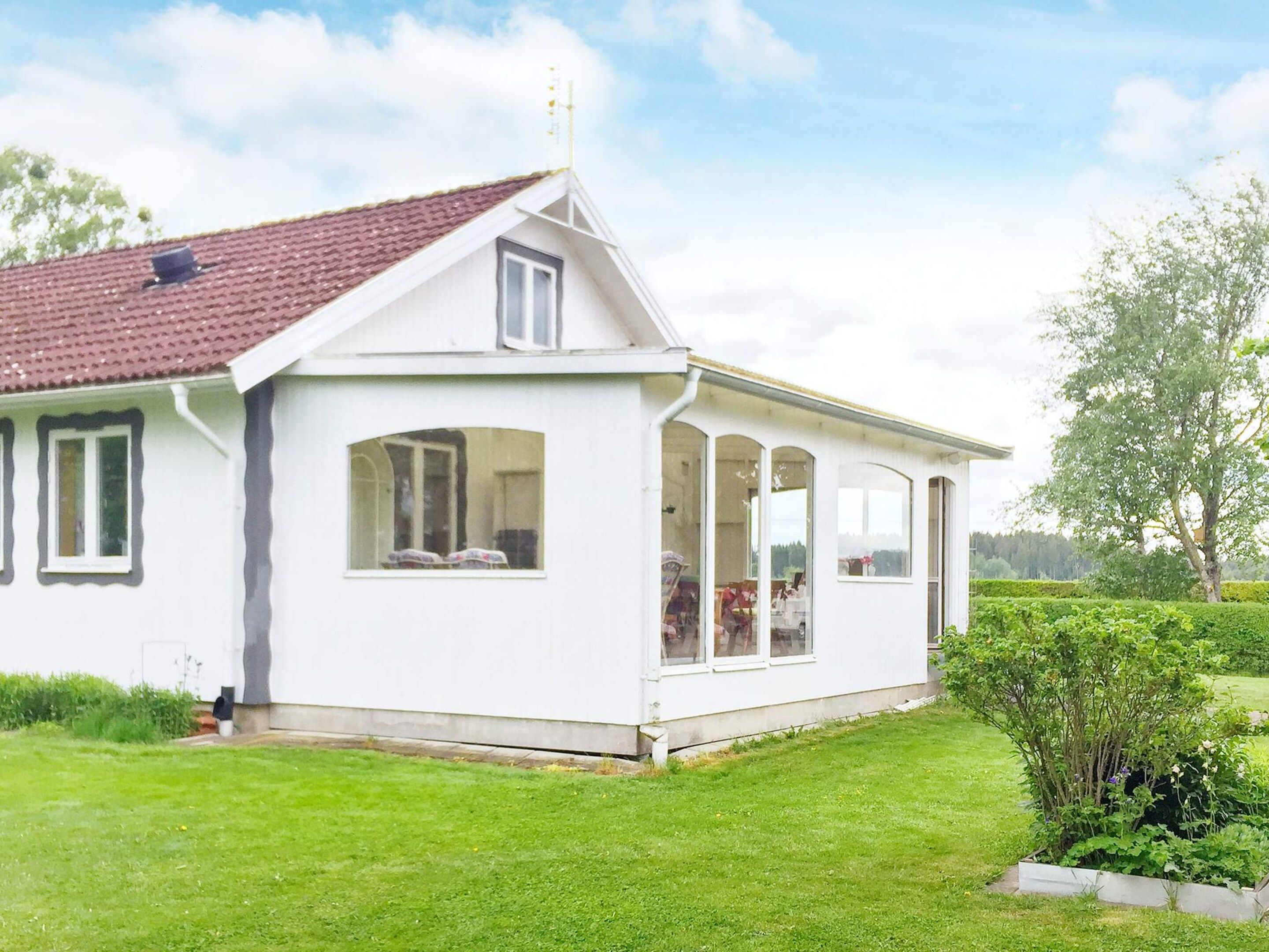 A white single-story house with a red-tiled roof, large windows, and a small garden.