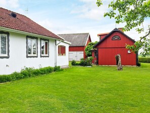 Une maison blanche, un hangar rouge et une construction à toit gris se dressent dans une cour verdoyante.