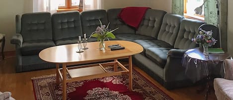 Un salon avec un canapé, une table basse, un tapis rouge à motifs et un vase rempli de fleurs.