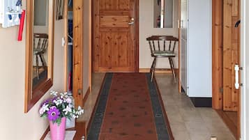 A hallway with a wooden door, a chair, a small table, and a vase of flowers.