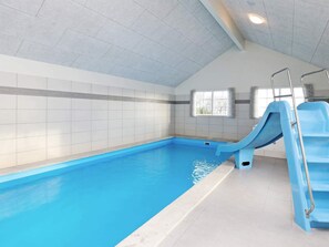 A swimming pool with a blue slide, tiled walls, and a window with curtains. - 5 Star Holiday Home in Frorup (Frørup)